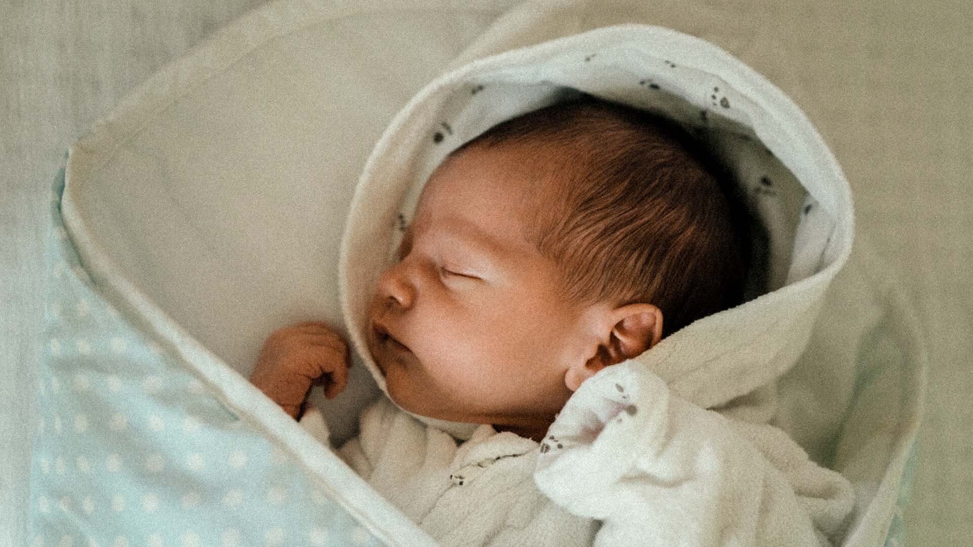 Bebis sover nerbäddad i ljusgrön filt med vita prickar 