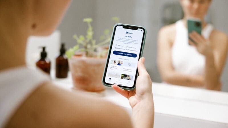Kvinna håller i en mobil och visar Capios app Kvinna håller i en mobil och visar Capios app