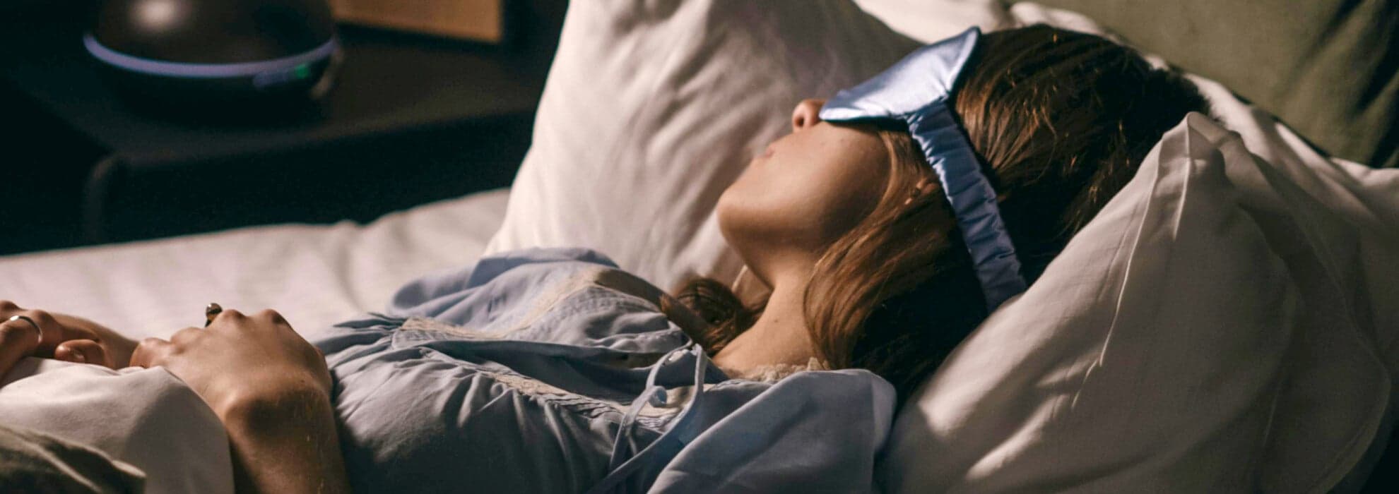 en kvinna som ligger i sängen och sover med en sovmask