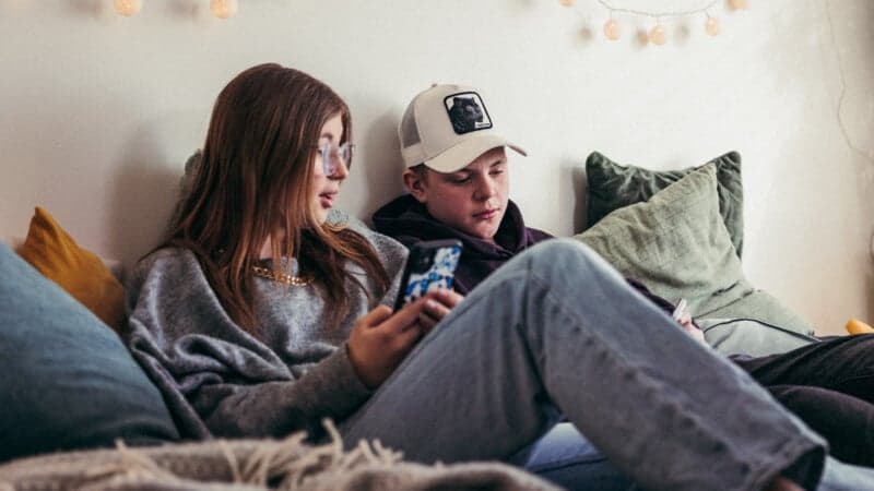 Ungdomar på säng tittar i mobiltelefon En tonårig tjej och kille på säng tittar i mobiltelefon