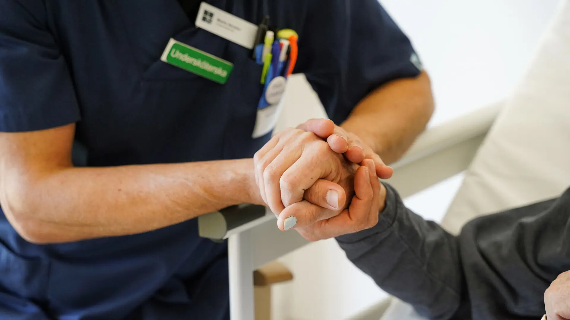 Undersköterska håller en sängliggande patient i handen.