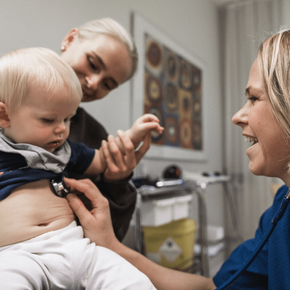 Doktor lyssnar på ett barns hjärta som sitter i knä på en vuxen