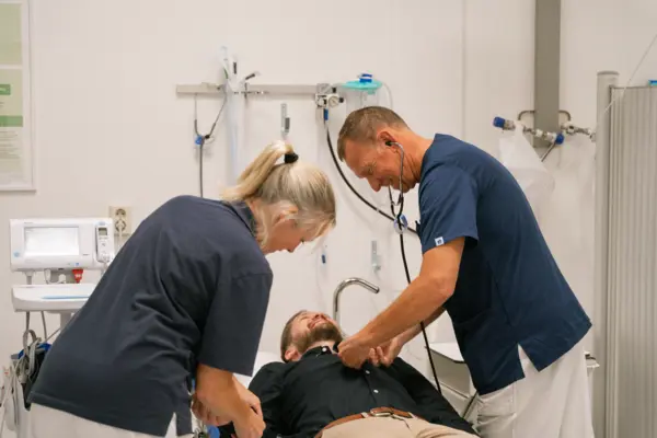 Läkare lyssnar på patient med stetoskop, sjuksköterska tar blodtryck