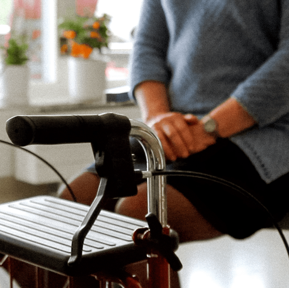 Rullator i förgrunden, kvinna i bakgrunden